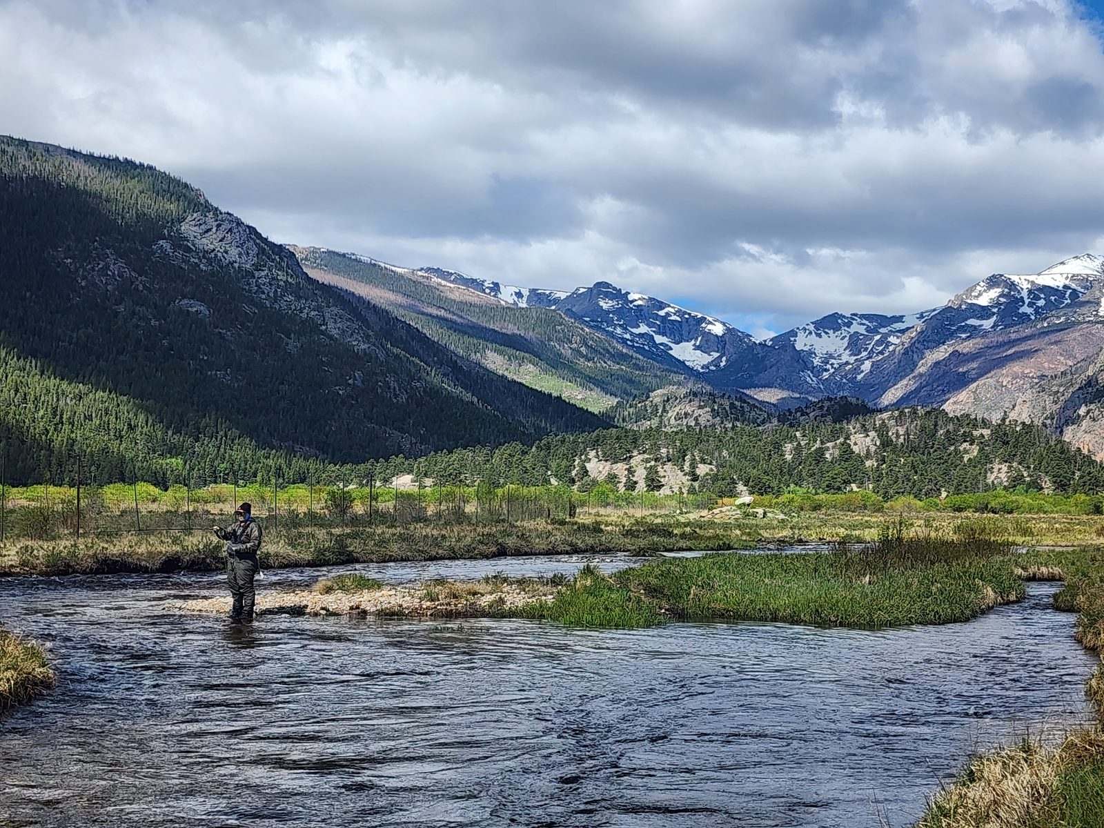 Niki Mosier fly fishing a high-country stream in Colorado, snow-capped Rocky Mountain peaks in the background